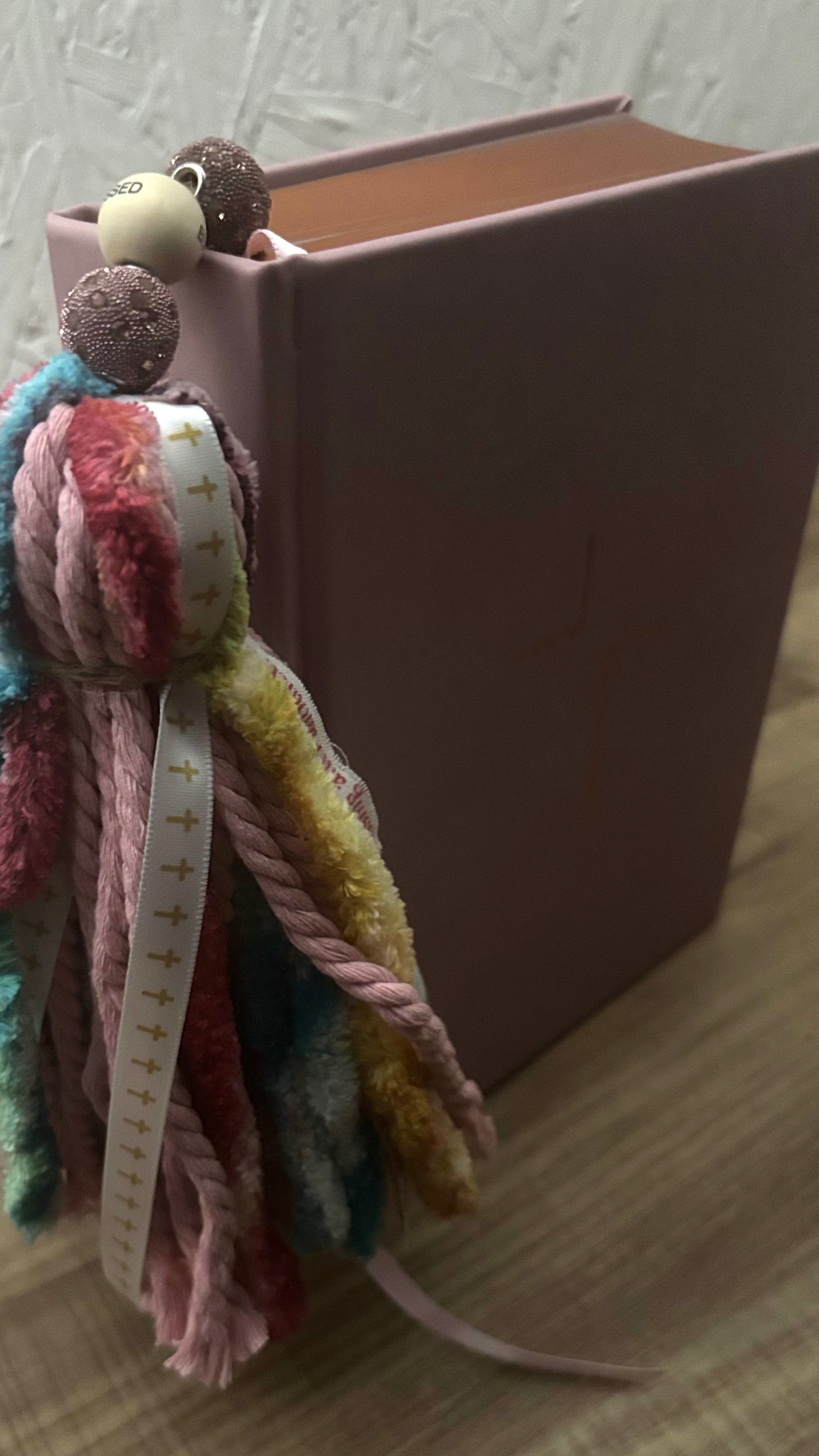 pink, multi color yarn, cross ribbon, and wooden bead bible bookmark, featured next to spine of Bible.
