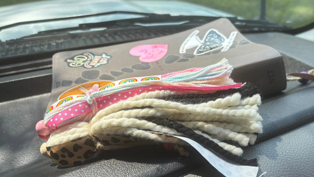 Bible on dash of vehicle with two bible tassels, featuring pink polka dot ribbon, and rainbow ribbon.