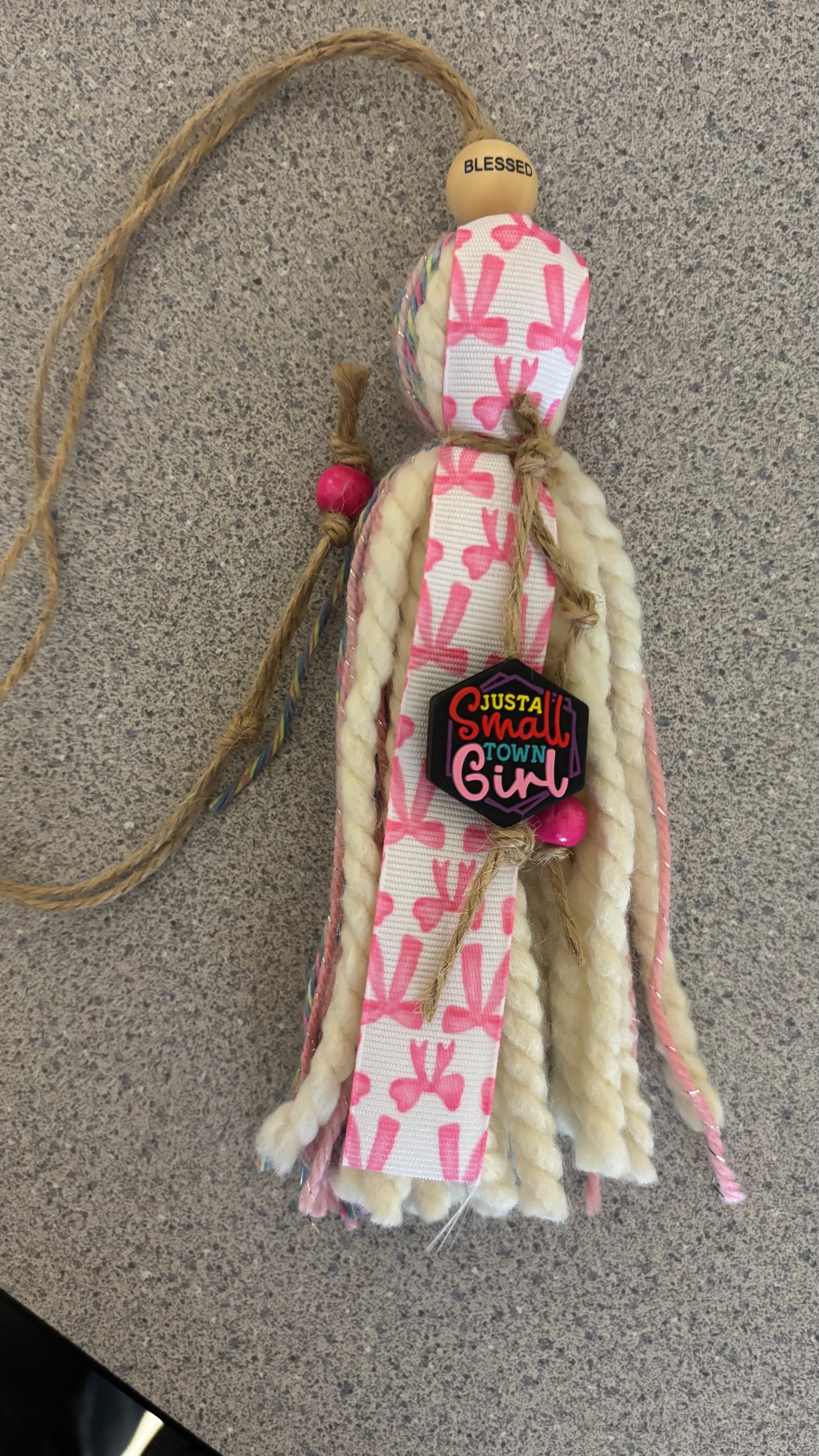 Decorative tassel with pink and white pattern and text on a neutral background